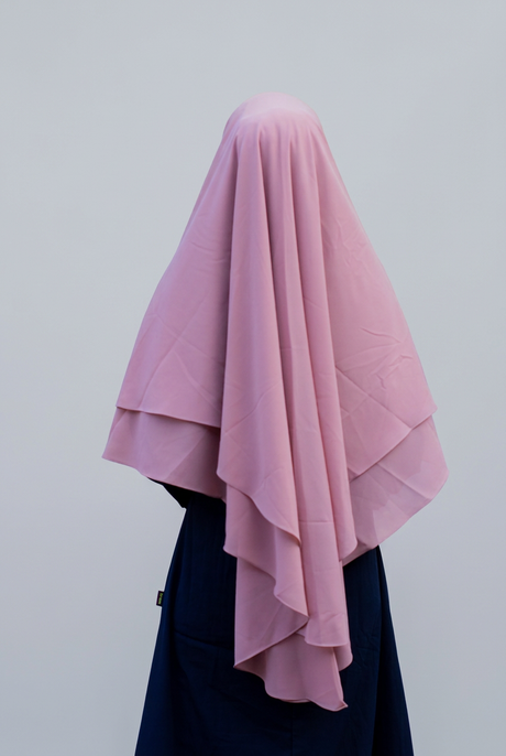 Roze Aliyah-khimar van achteren, met twee lagen en lange vallende plooien tegen een lichtgrijze achtergrond.